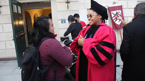 woman in a doctoral graduation robe speaking with another woman