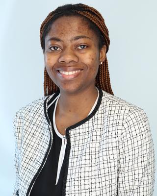 Headshot of Francisca facing the viewer with a blue background wearing a black and white suitjacket