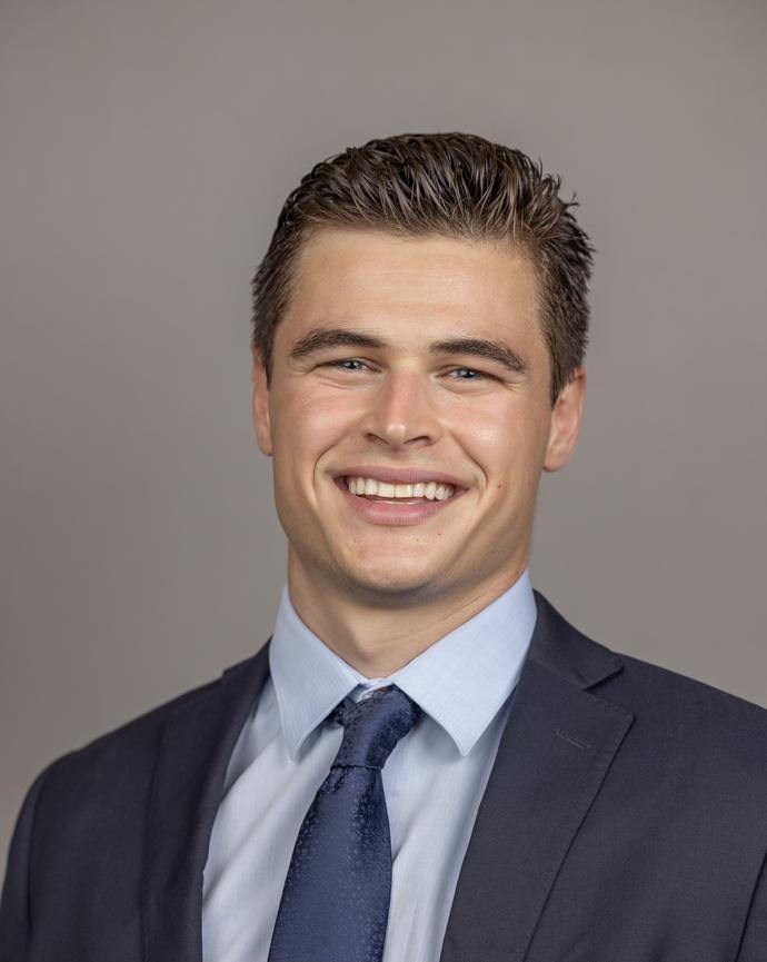 headshot of Daniel wearing a navy colored suit, smiling and facing the camera